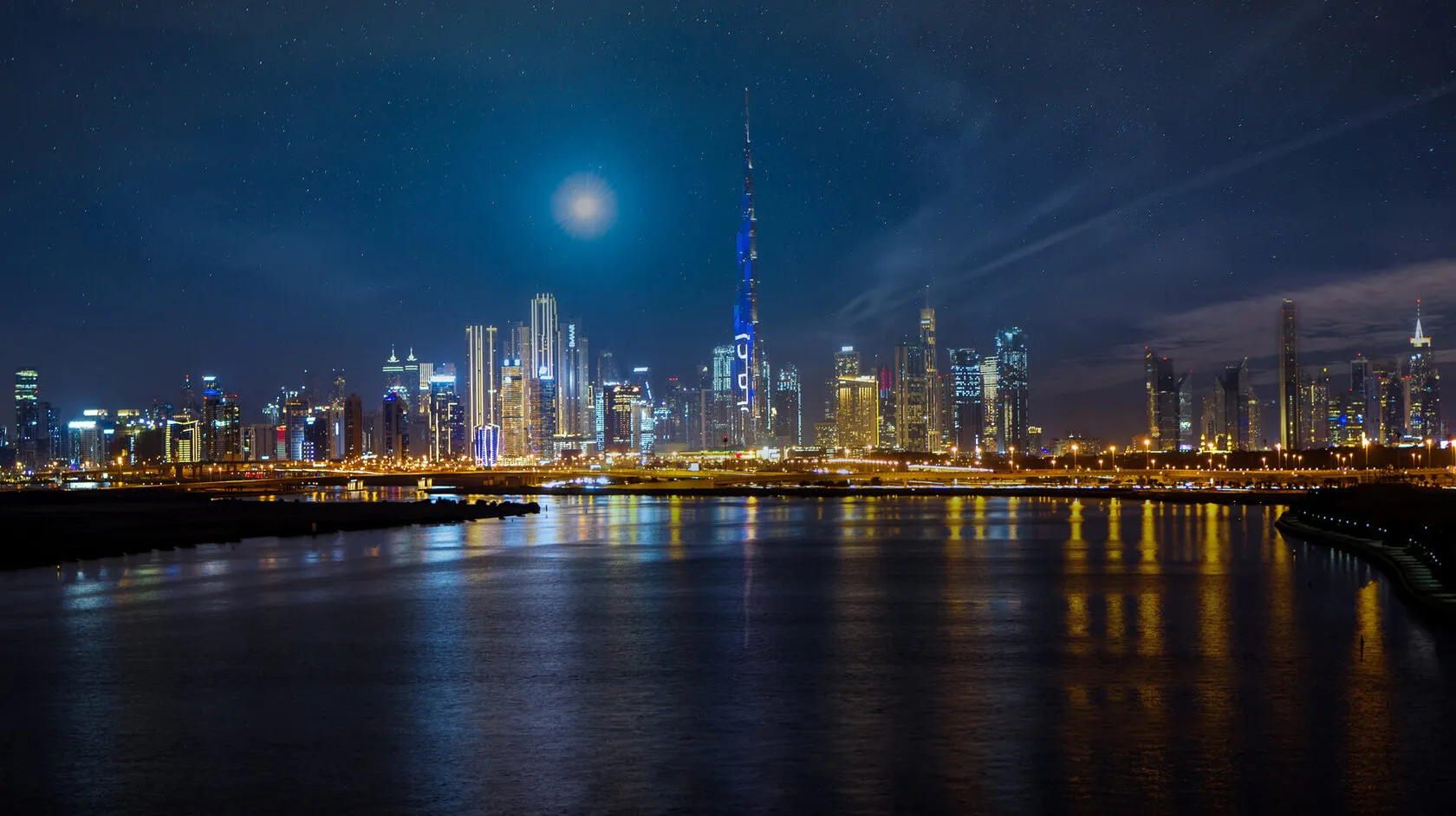 Dubai Creek at night with the Downtown Dubai skyline beyond and city lights on the water