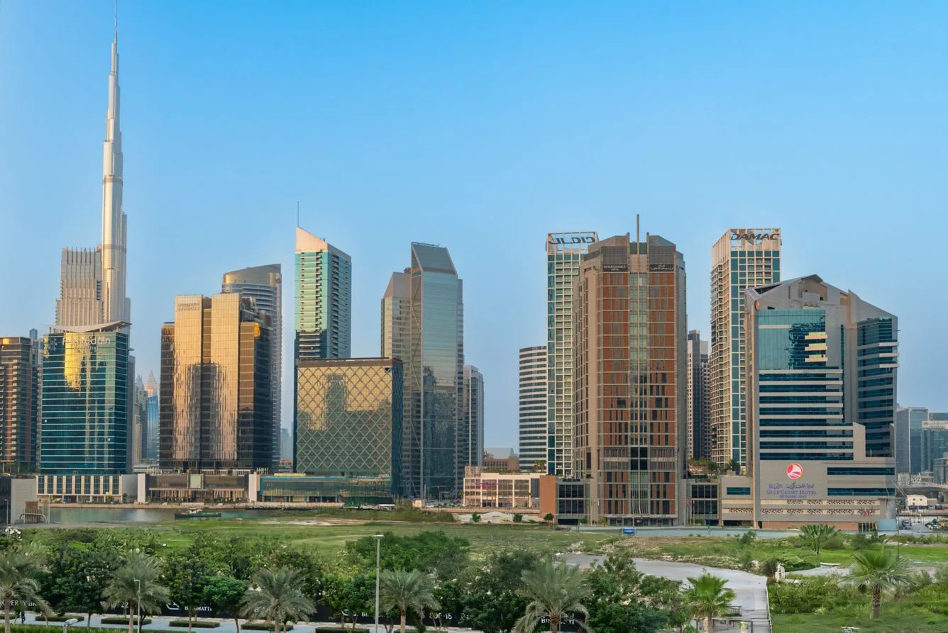 Dubai high-rise towers and green parkland in daylight with Burj Khalifa on the horizon